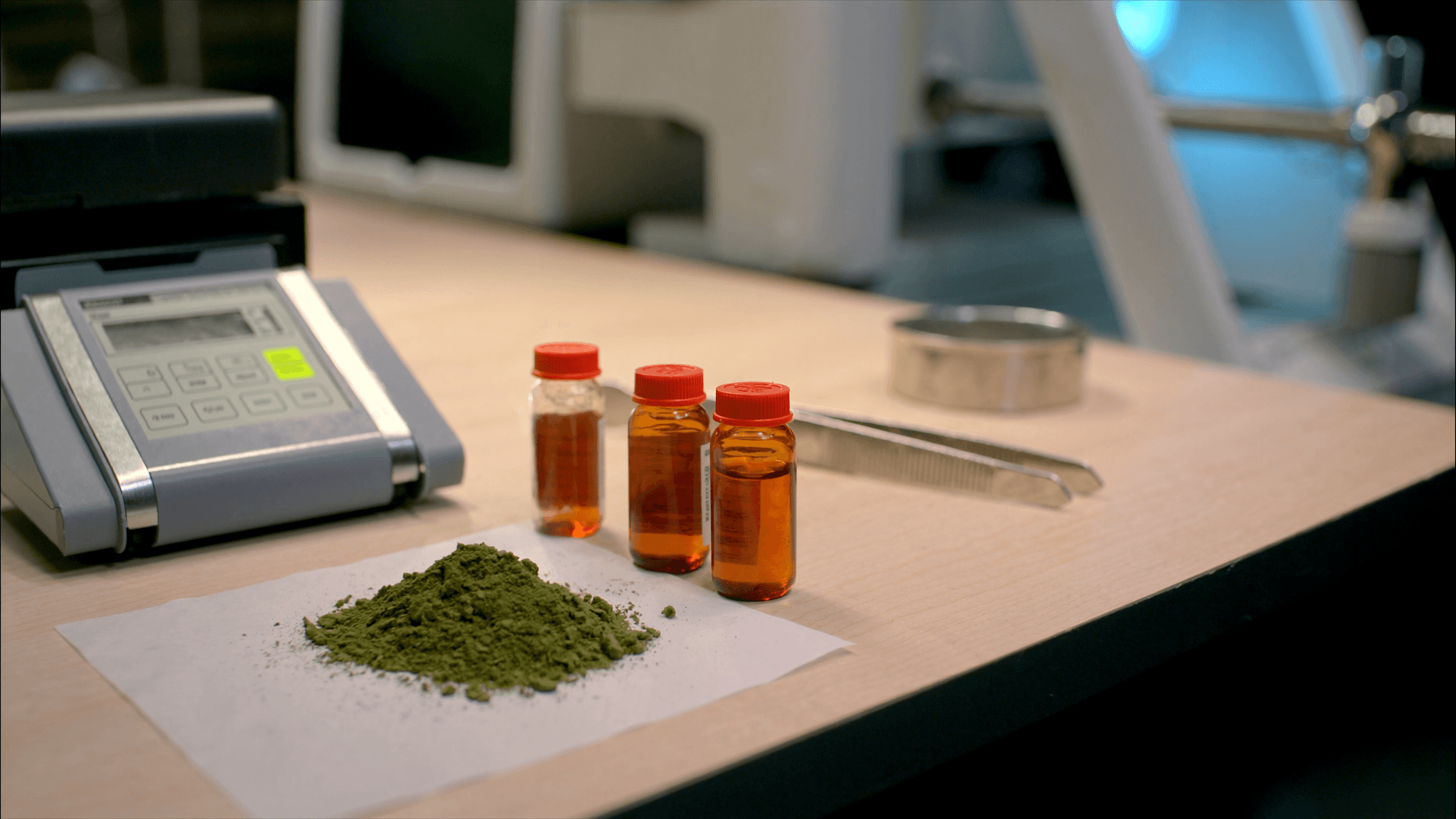Kratom leaf powder being weighed on an analytical balance with alkaloid extraction vials