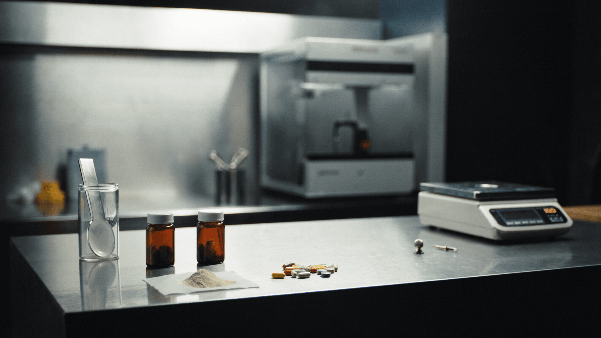 Dietary supplement capsules, tablets, and powder on an analytical balance with ICP-MS in the background